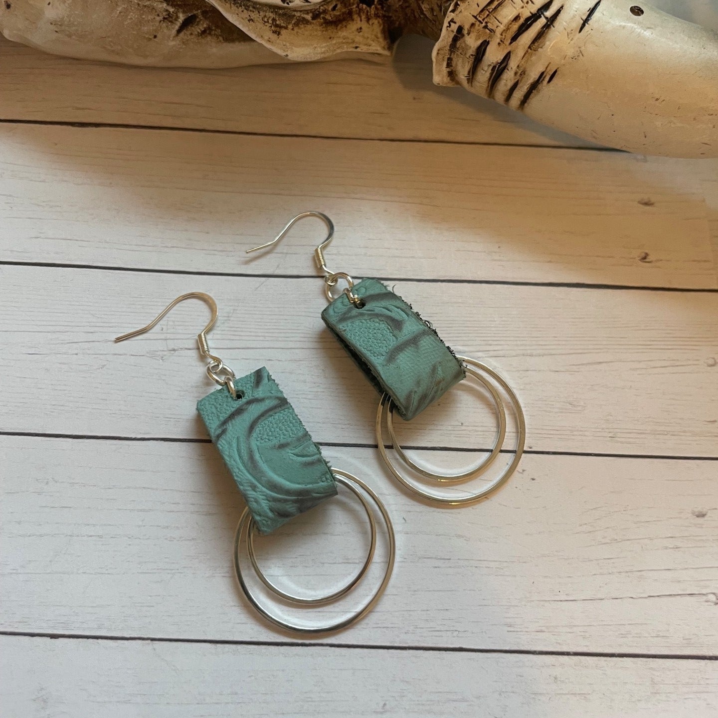Pair of green earrings on a wooden surface with natural elements.