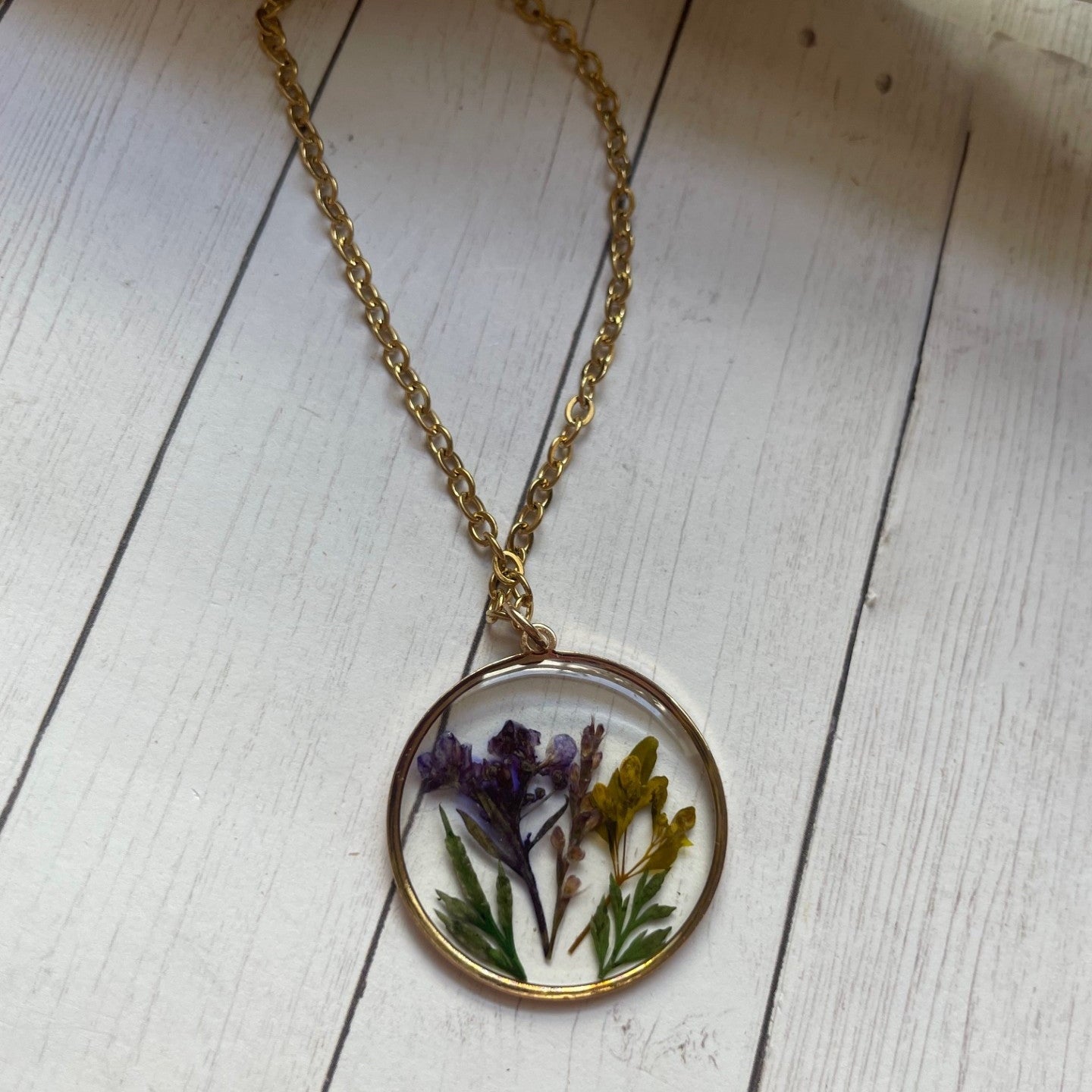 Necklace with a round pendant featuring pressed flowers on a wooden surface