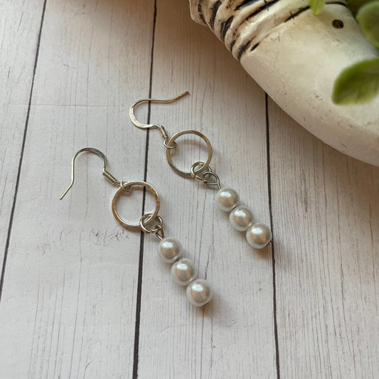 Pearl drop earrings on a wooden surface with a shell and plant in the background