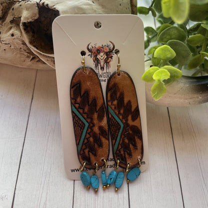 Leopard print earrings with turquoise accents on a white card, placed on a wooden surface with a plant in the background.