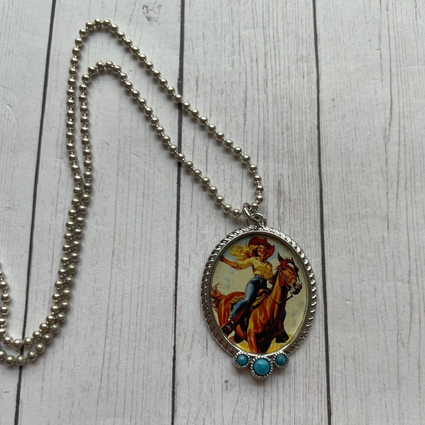 Necklace with a pendant featuring a horse and rider on a wooden surface