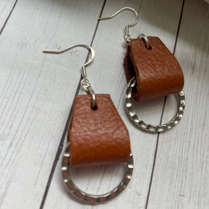 Brown leather hoop earrings on a light wooden surface