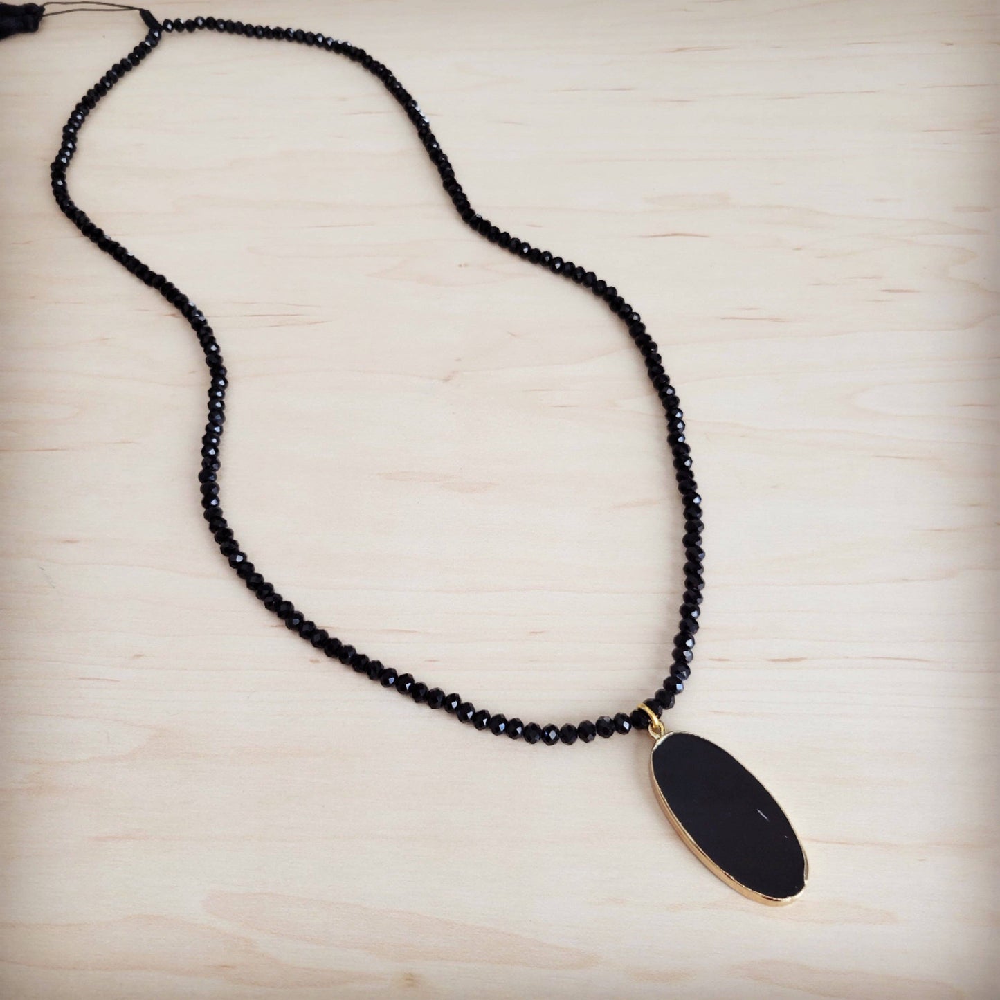 Black beaded necklace with a gold pendant on a light wooden surface