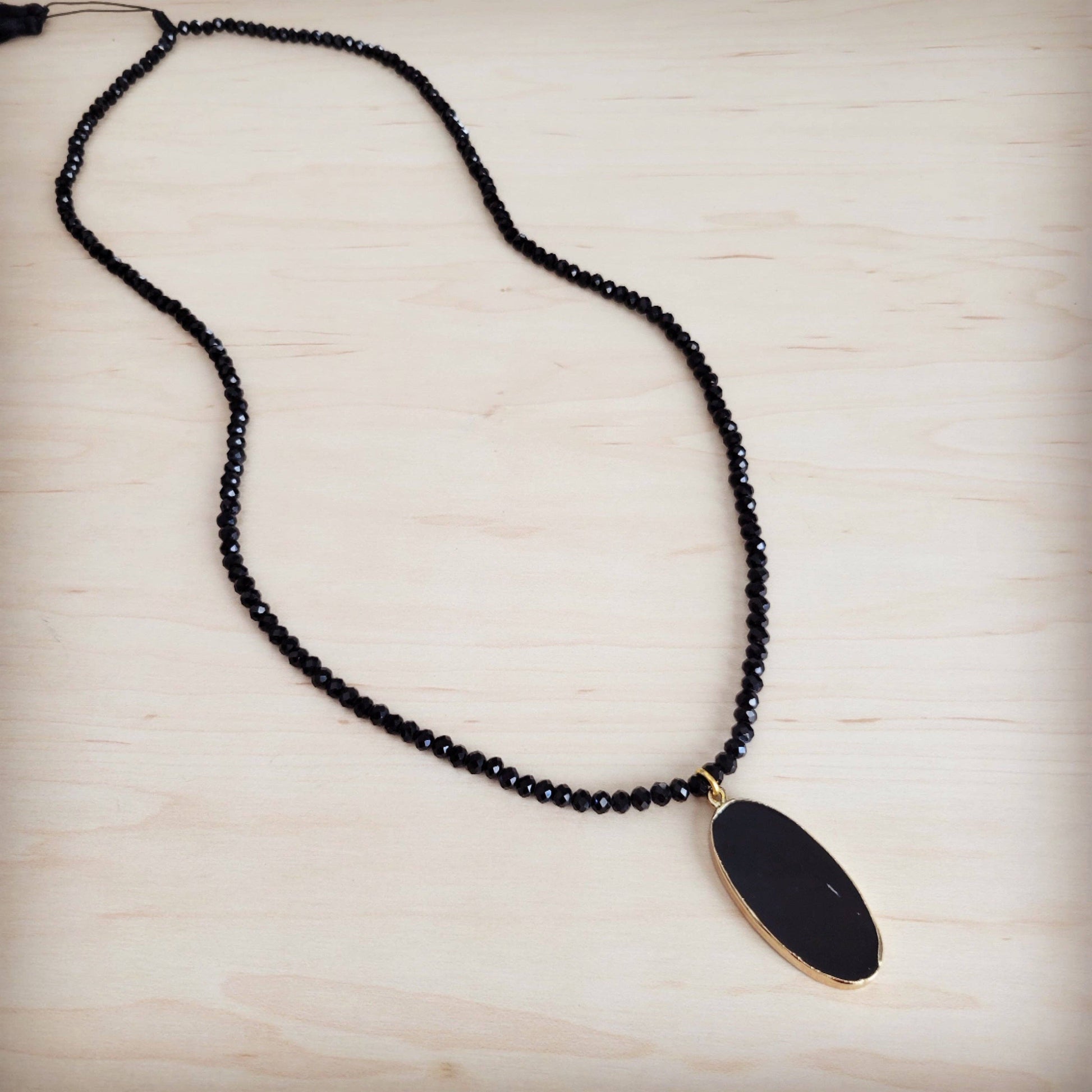 Black beaded necklace with a gold pendant on a light wooden surface