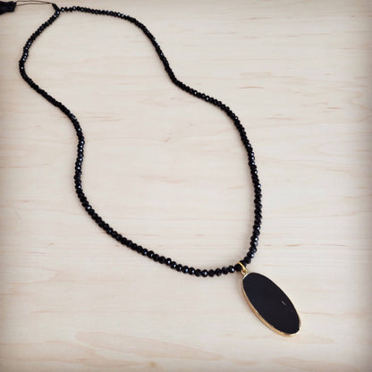 Black beaded necklace with a gold pendant on a light wooden surface