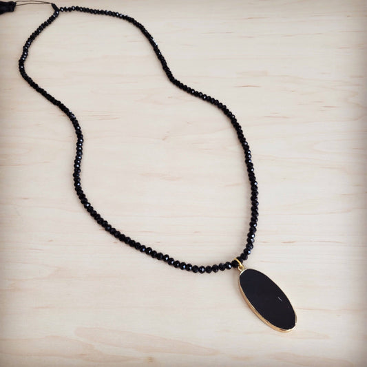 Black beaded necklace with a gold pendant on a light wooden surface