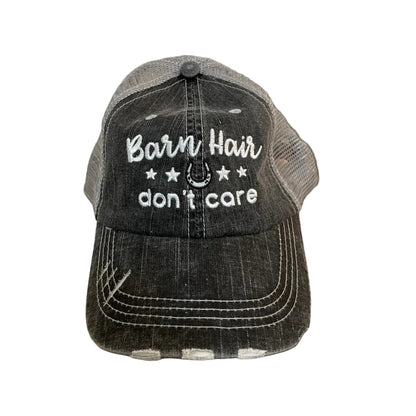 Black and gray cap with 'Barn Hair don't care' text on a wooden surface with hay bales in the background