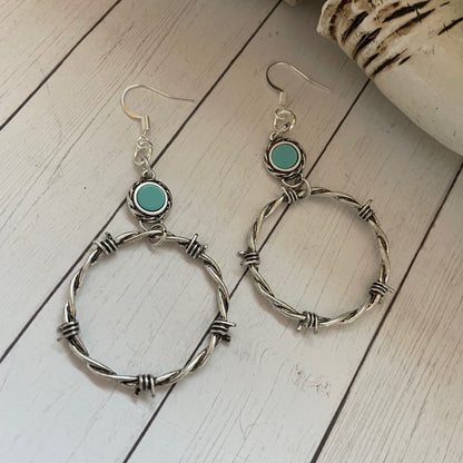 Silver hoop earrings with turquoise stones on a wooden surface