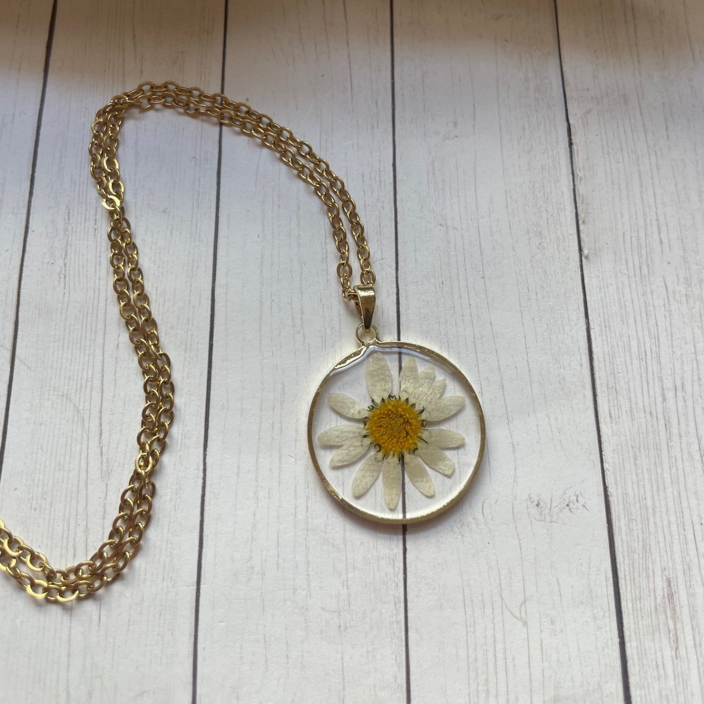Gold necklace with a round pendant featuring a pressed flower on a wooden surface