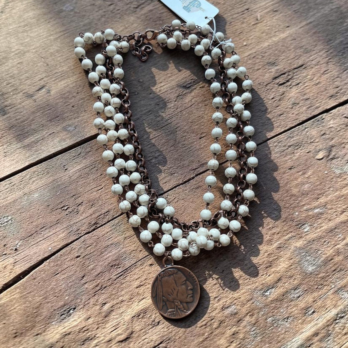 Necklace with white beads and a coin pendant on a wooden surface