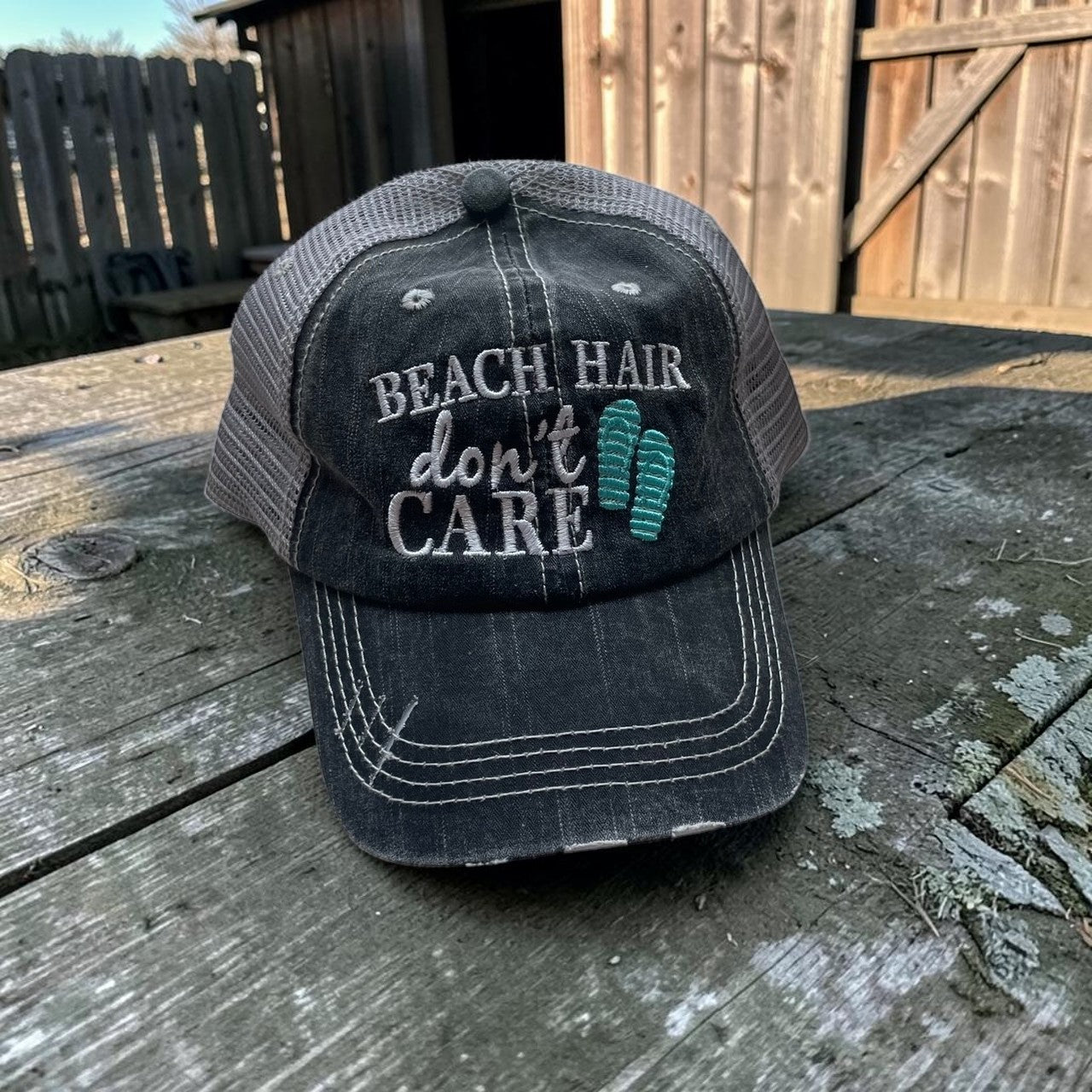 Black cap with 'Beach Hair Don't Care' text on a wooden surface