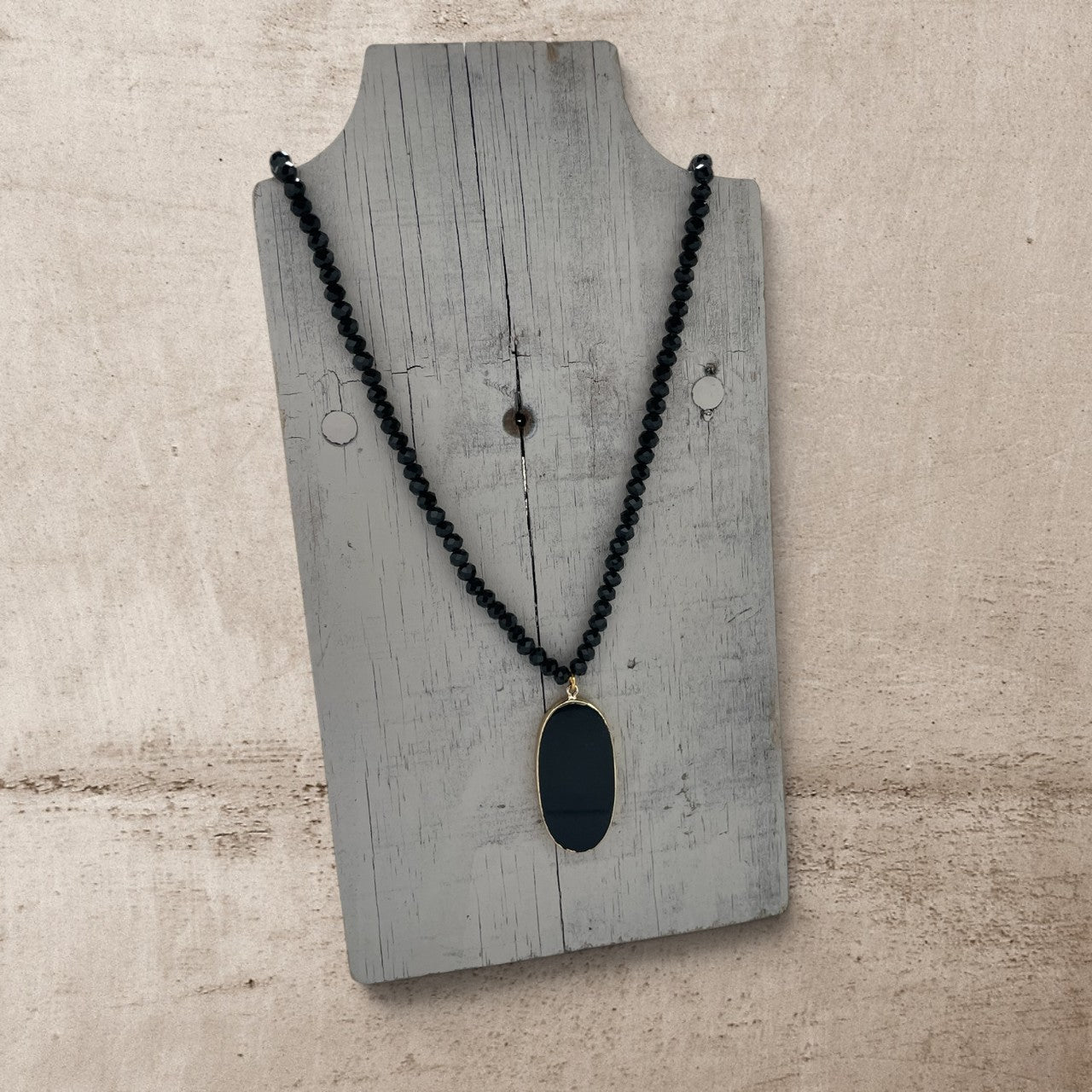 Black beaded necklace with a pendant on a wooden display stand.