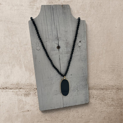 Black beaded necklace with a pendant on a wooden display stand.