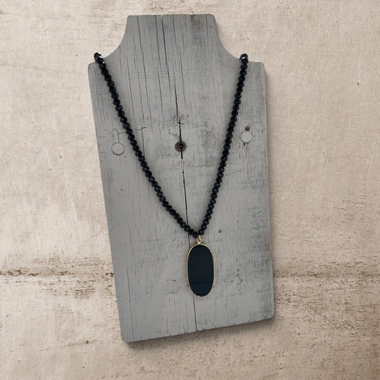 Black beaded necklace with a pendant on a wooden display stand.