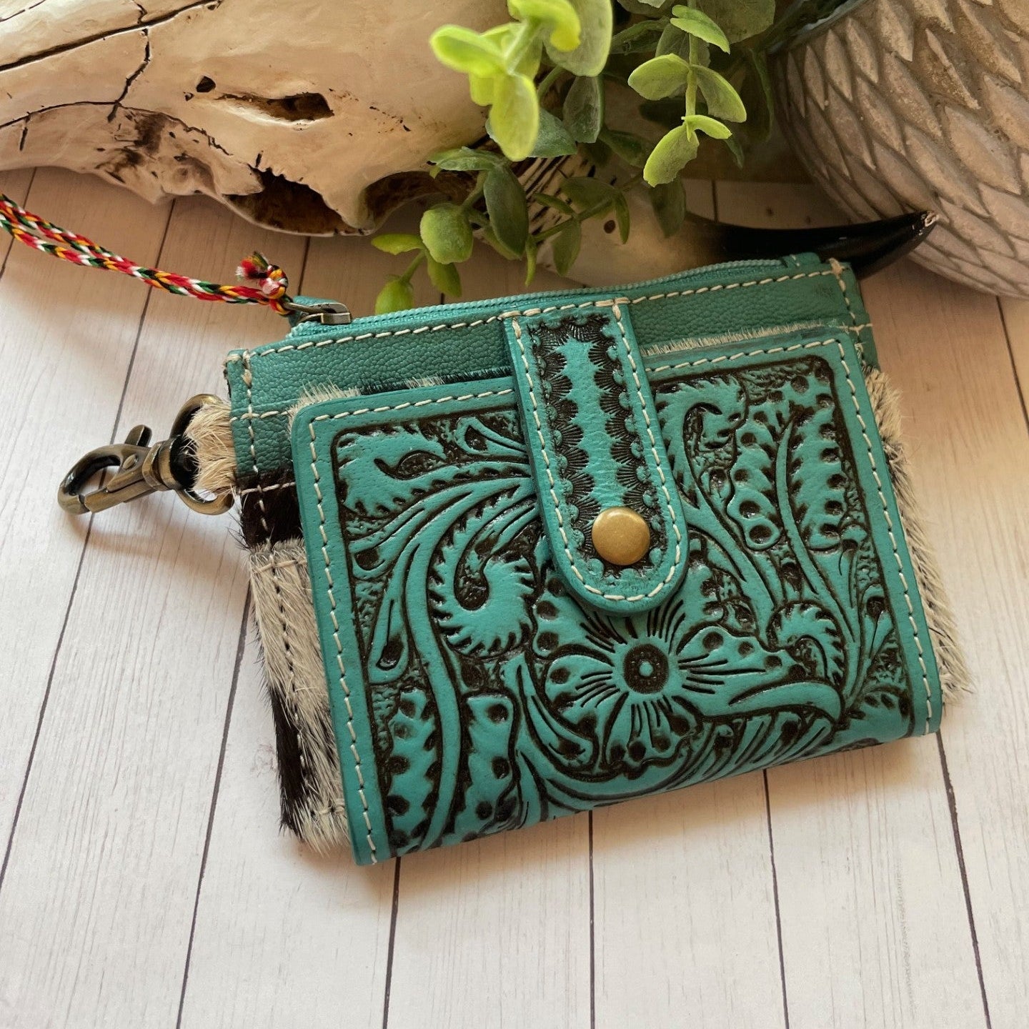 Turquoise leather wallet with intricate patterns on a wooden surface with plants in the background