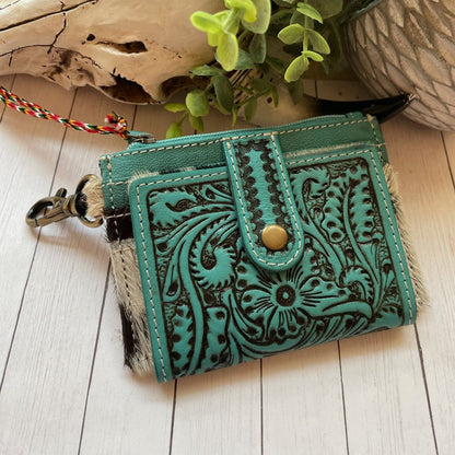 Turquoise leather wallet with intricate patterns on a wooden surface with plants in the background