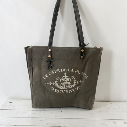 Gray tote bag with 'Le Cafe de la Place Provence' logo on a white background