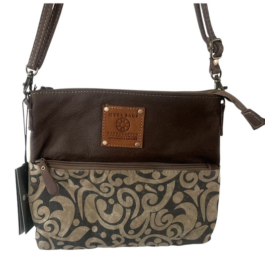 A women's crossbody bag featuring a dark brown leather top half with a tan brand patch, and a lower half with a beige and dark gray damask pattern, shown on a white background.
