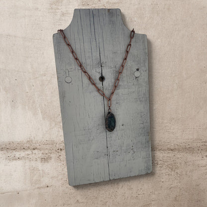 Necklace with a pendant on a rustic wooden stand against a beige background