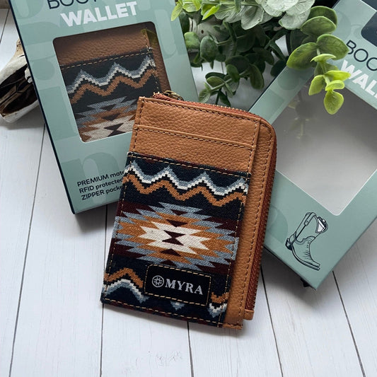 Brown wallet with tribal pattern and 'MYRA' branding on a white surface with packaging and greenery.