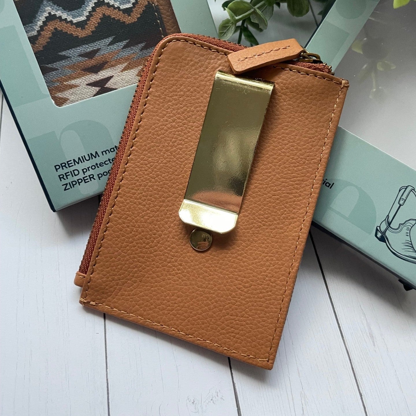 Brown leather wallet with gold clip on a white surface with greenery in the background