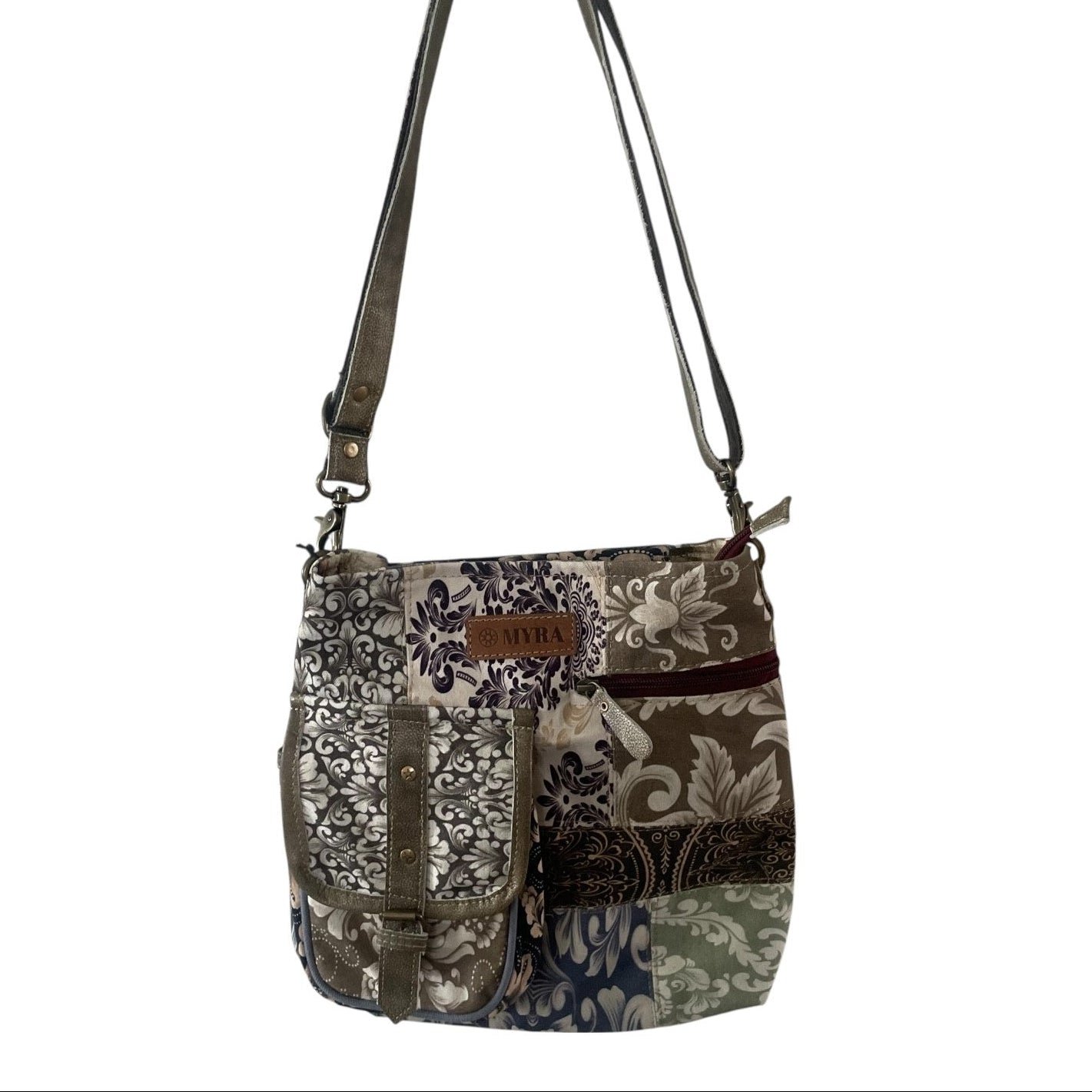 A patchwork crossbody bag with a floral and paisley pattern in beige, brown, navy, and green, featuring dark brown faux-leather straps and a small brown leather brand patch that reads 'SUNSET'.