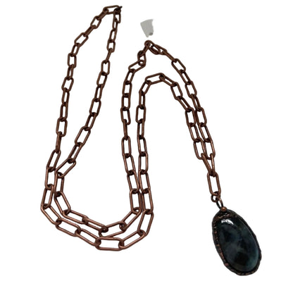 Long chain necklace with a black pendant on a white surface, featuring a brand tag.