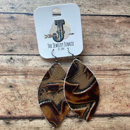 Pair of brown and black patterned earrings with a branded card on a wooden surface