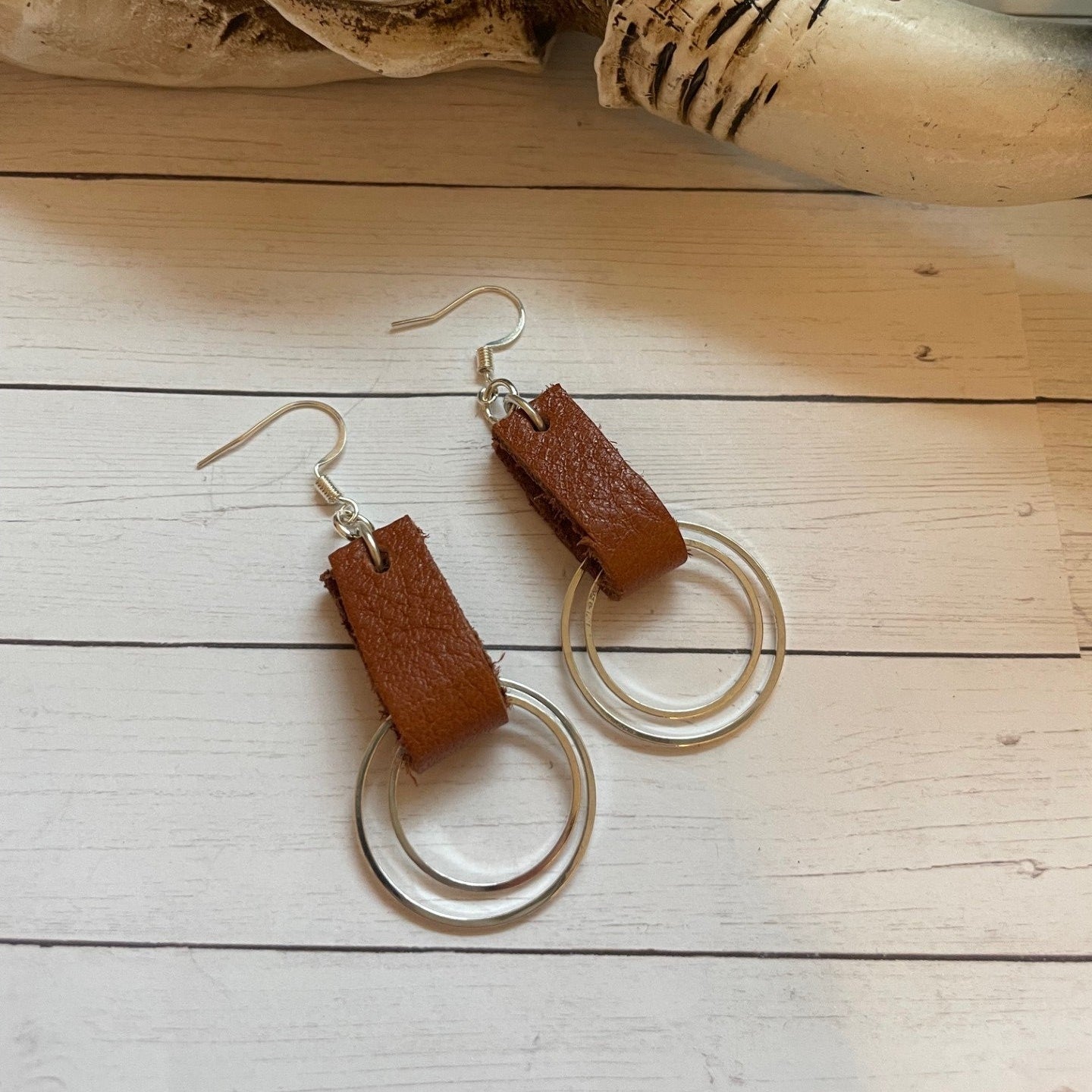 Brown leather earrings with silver loops on a wooden surface