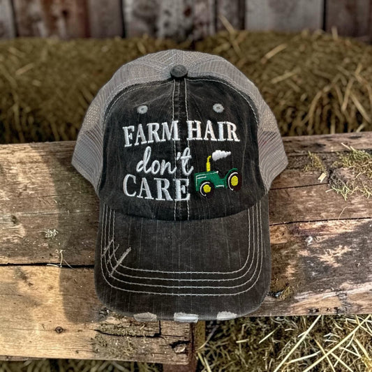 Cap with 'Farm Hair Don't Care' text and tractor graphic on a wooden surface with hay in the background
