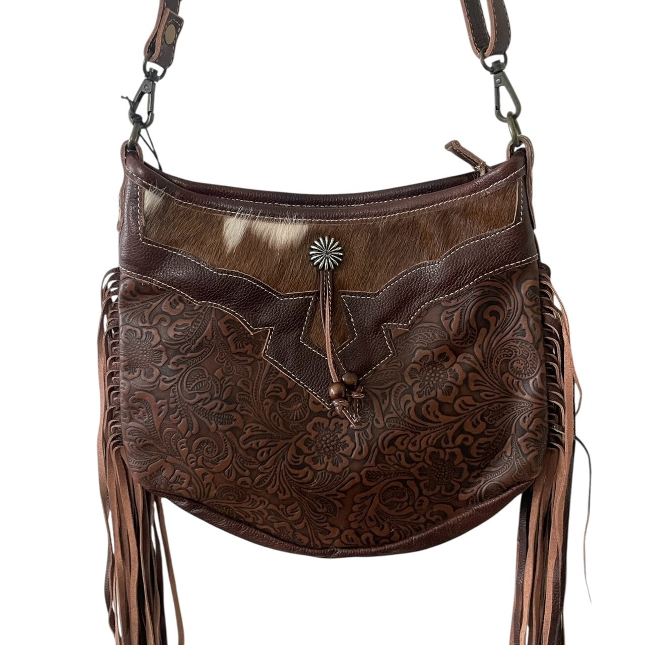 Brown leather handbag with intricate patterns and fringes on a white background
