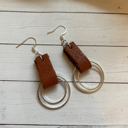 Brown leather earrings with silver hooks on a wooden surface