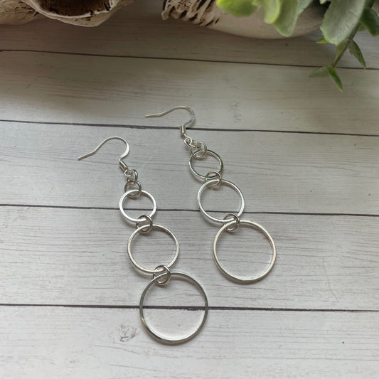 Silver circular earrings on a light wooden surface with a plant in the background