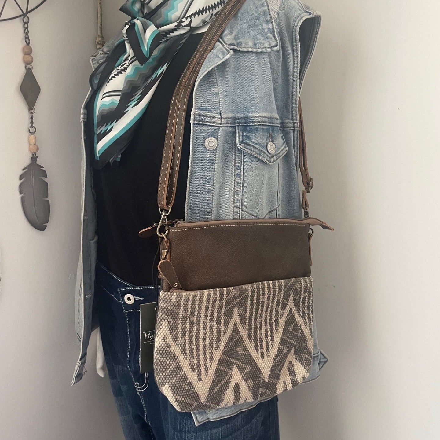 Mannequin wearing a denim vest, black shirt, and patterned scarf with a brown crossbody bag.