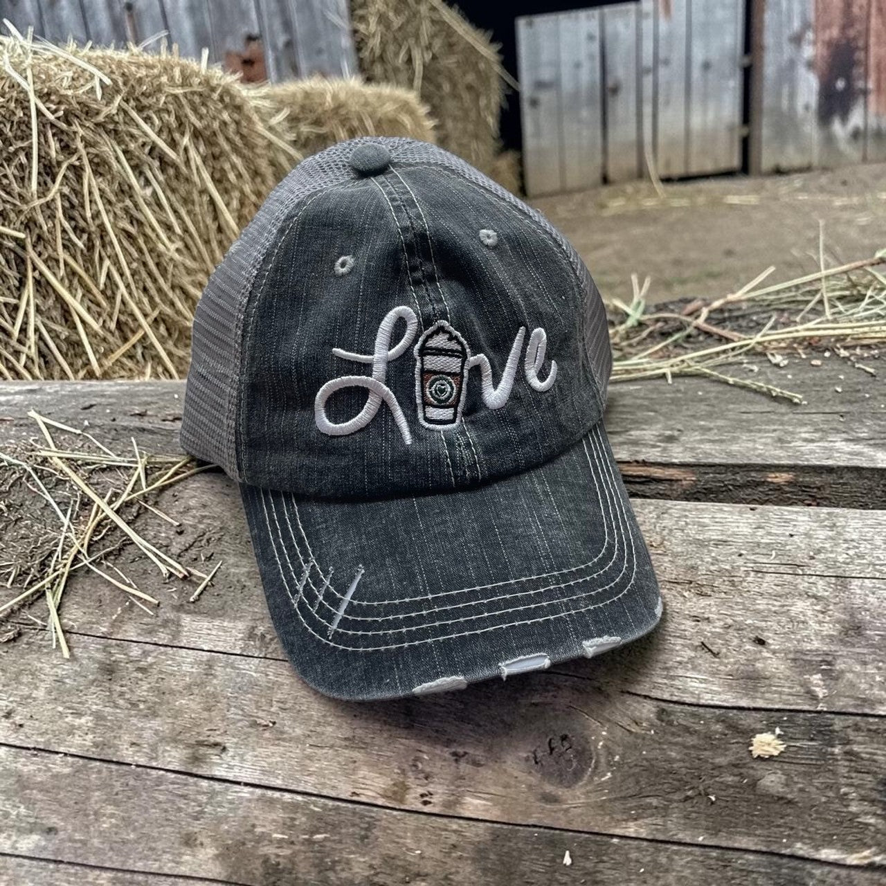 Black cap with 'love' embroidery on a wooden surface with hay bales in the background