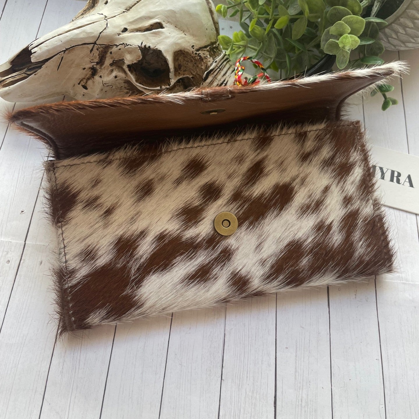 Cowhide clutch bag with a skull and plant on a wooden surface