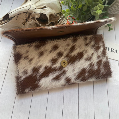 Cowhide clutch bag with a skull and plant on a wooden surface
