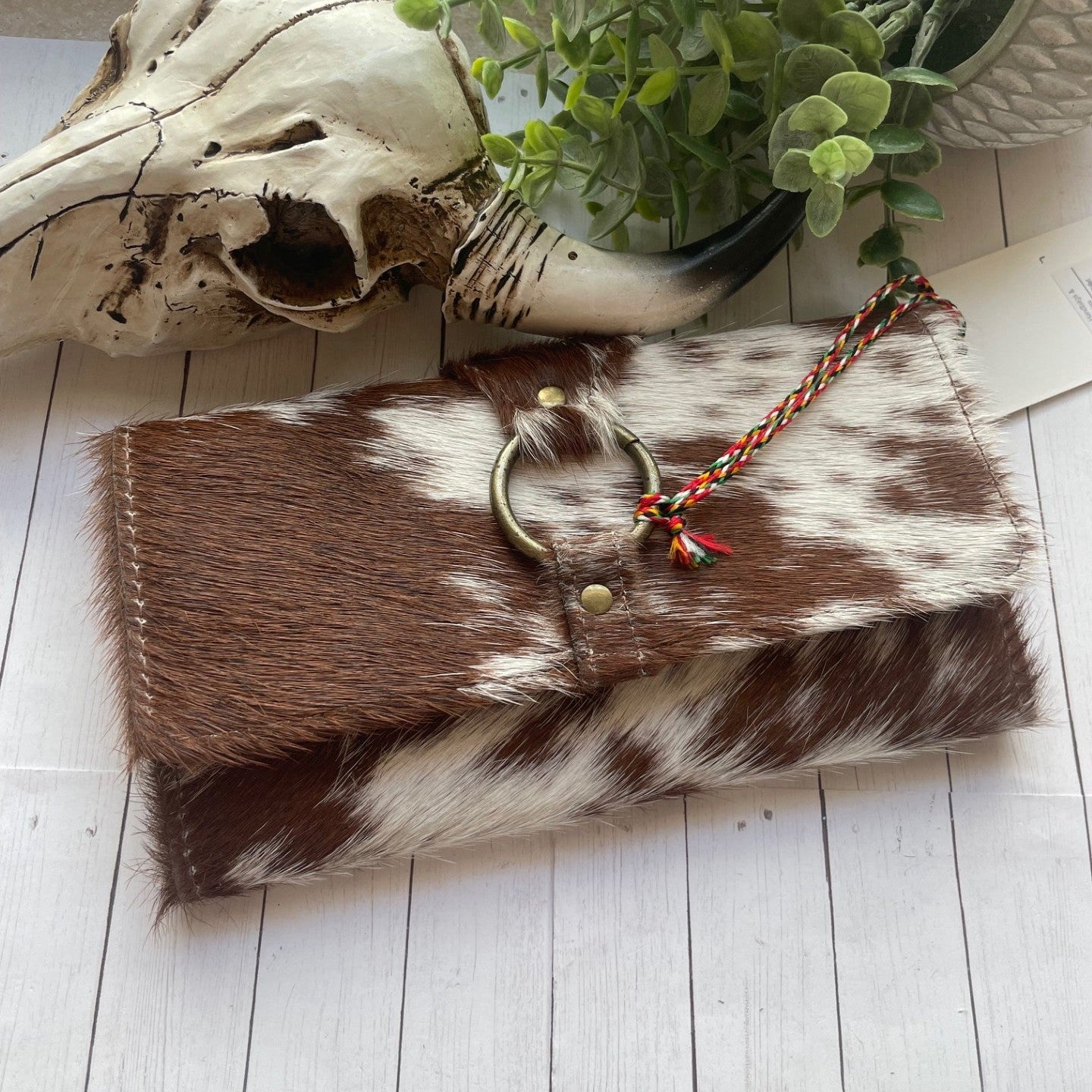Brown and white cowhide wallet pouch with decorative elements on a light wooden surface.