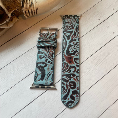 Patterned turquoise leather watch strap on a wooden surface with a plant in the background