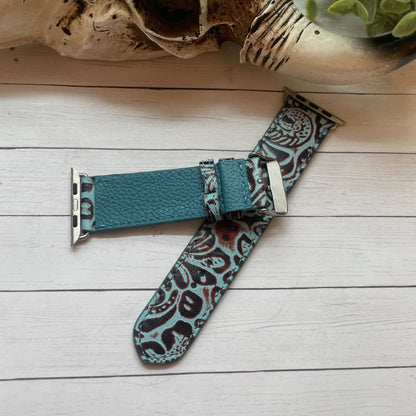 Teal patterned watch strap on a wooden surface with a skull and plants in the background