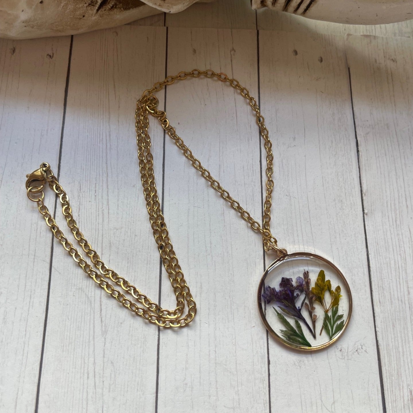 Gold necklace with a pendant featuring pressed flowers on a wooden surface