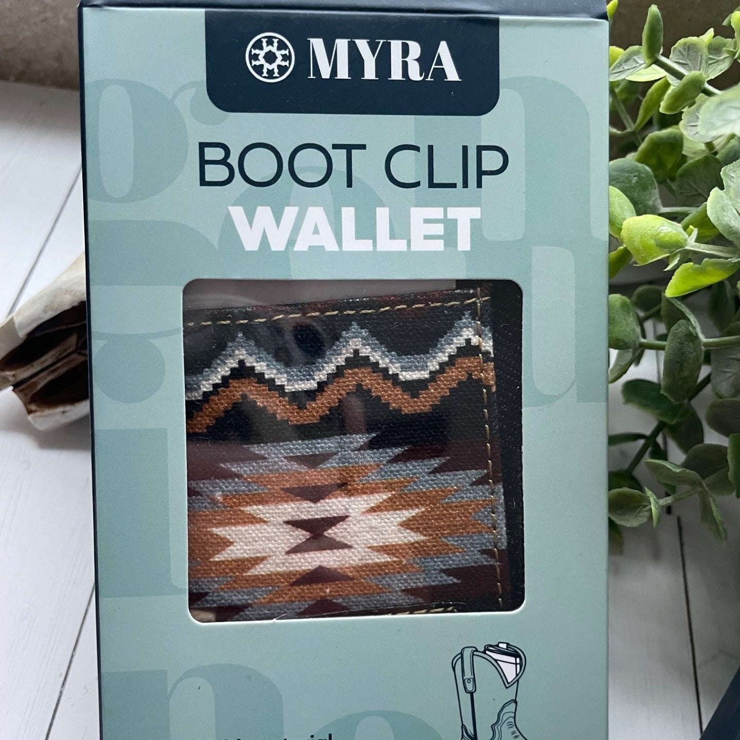 MYRA boot clip wallet packaging on a light surface with a plant in the background