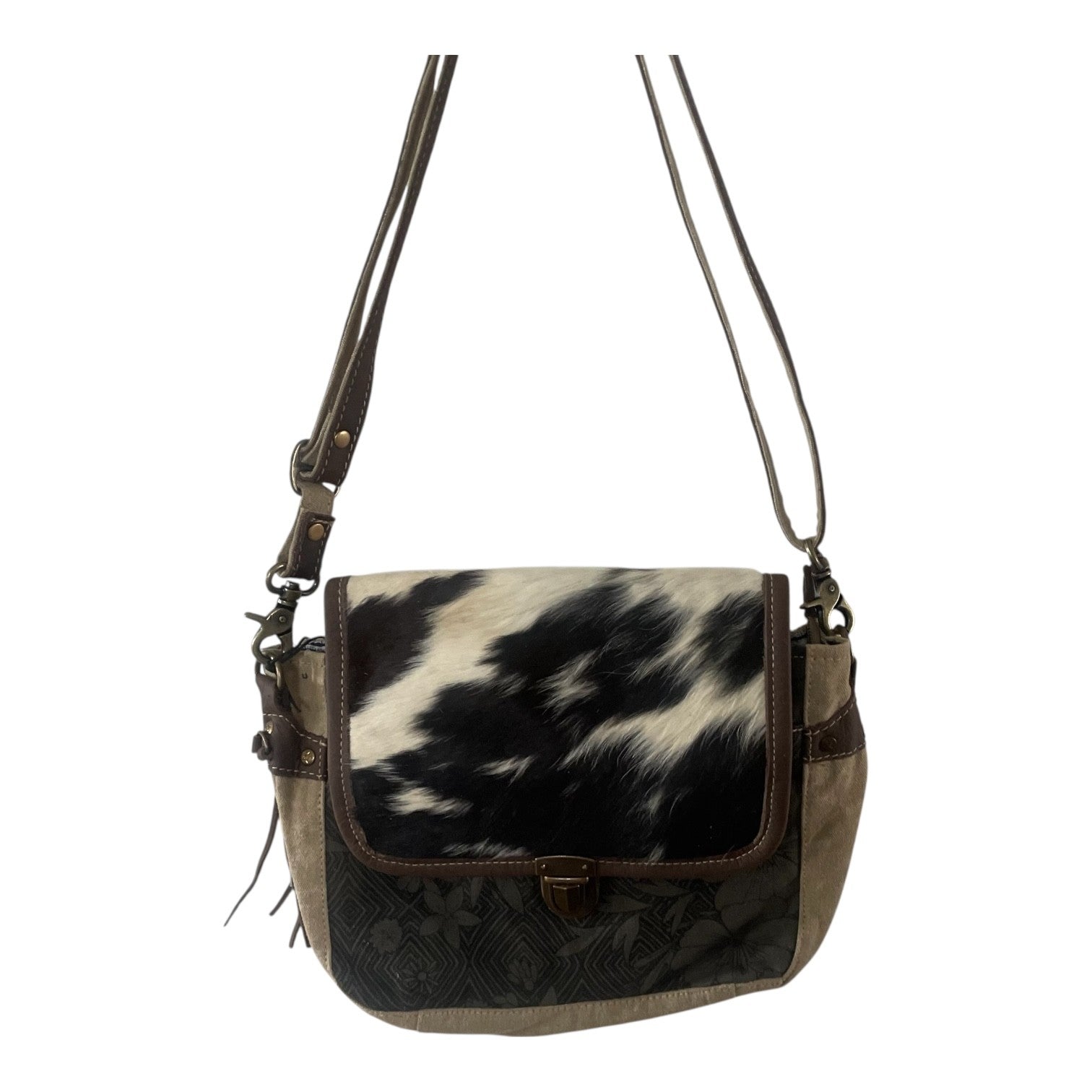 A shoulder bag with a black and white cowhide pattern on the front flap, dark brown leather trim, and a dark brown embossed pattern on the lower front panel, featuring a brown leather strap and a small gold-tone clasp.