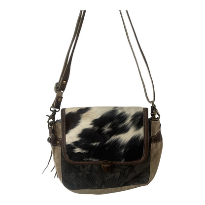A shoulder bag with a black and white cowhide pattern on the front flap, dark brown leather trim, and a dark brown embossed pattern on the lower front panel, featuring a brown leather strap and a small gold-tone clasp.