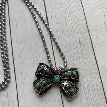 Necklace with a bow-shaped pendant featuring turquoise stones on a wooden surface