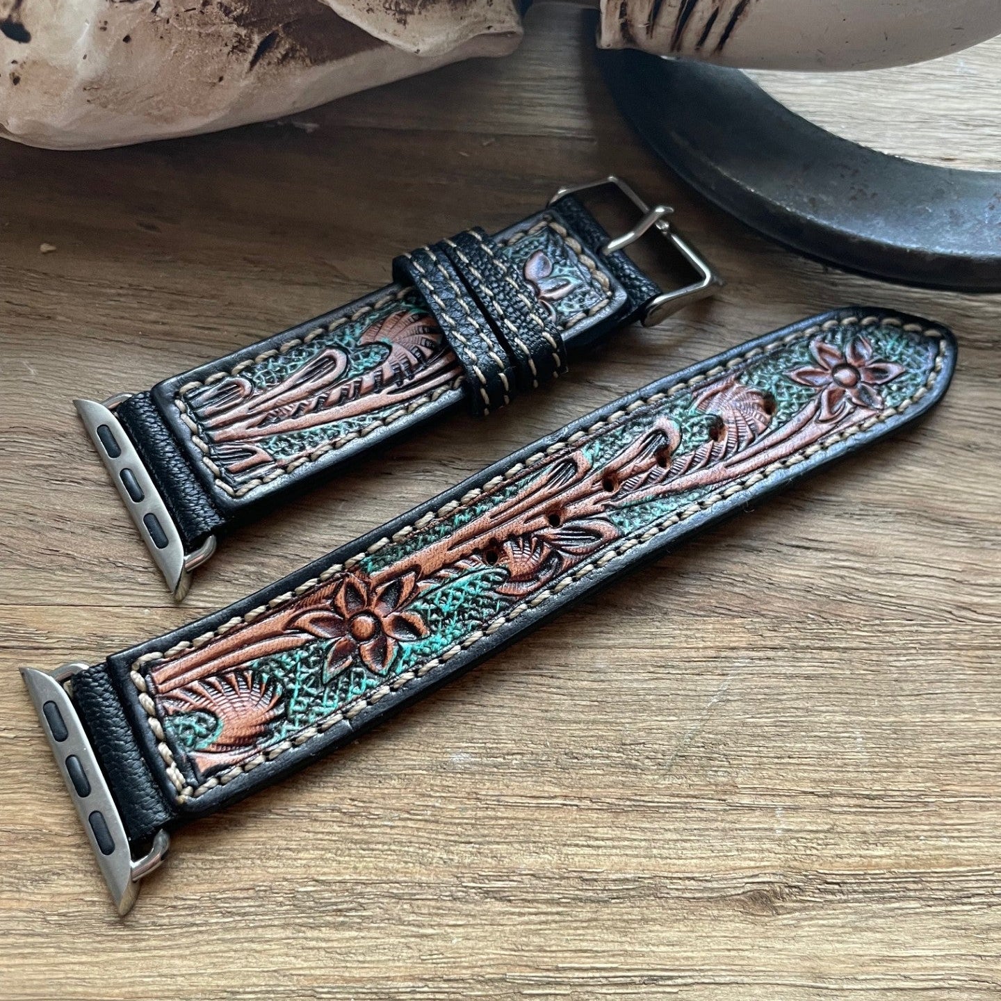 Decorative leather watch strap with floral patterns on a wooden surface