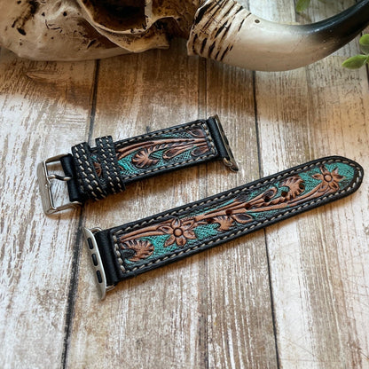 Two intricately designed leather watch straps on a wooden surface with a skull and horns in the background.