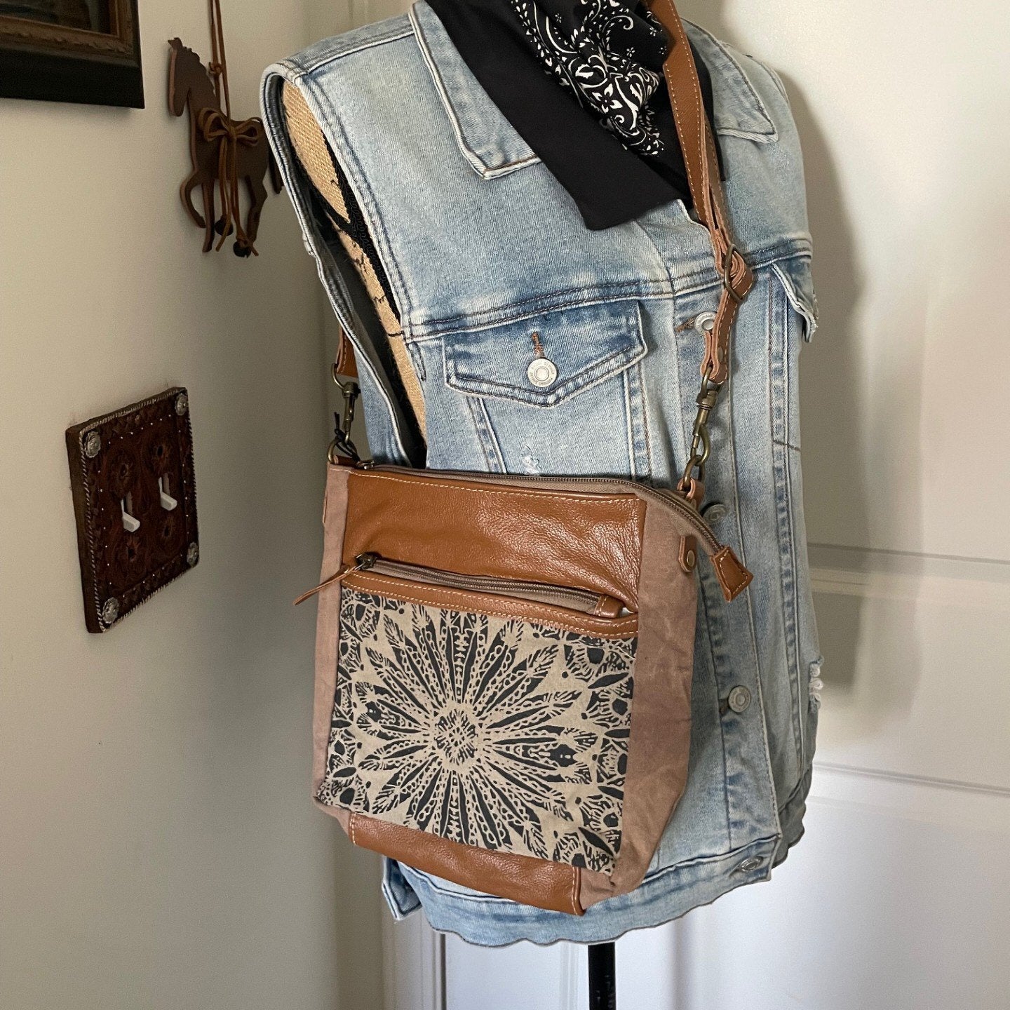 Mannequin wearing a denim vest with a brown leather bag featuring lace detailing.