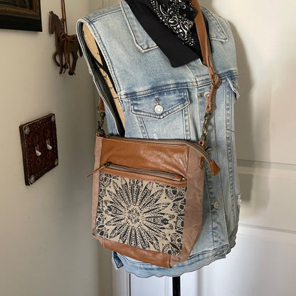Mannequin wearing a denim vest with a brown leather bag featuring lace detailing.