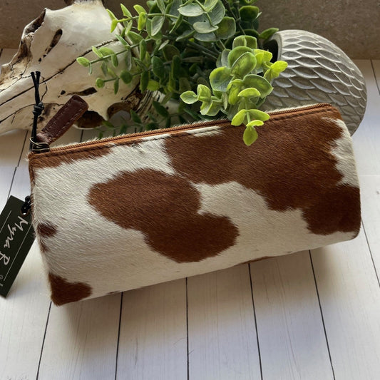 Cow print pouch with a plant on a wooden floor, next to a skull and antlers.